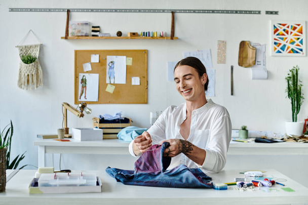Un joven sonríe mientras cose meticulosamente una prenda de vestir en su atelier iluminado. Centrado en la sostenibilidad, da nueva vida a las prendas desechadas. - Foto, imagen