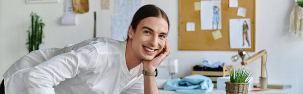 Un joven con una camisa blanca sonríe brillantemente mientras trabaja en su taller de restauración de ropa. - Foto, imagen