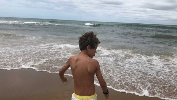 Boy backing out from sea shore water, afraid of getting wet - Photo, Image