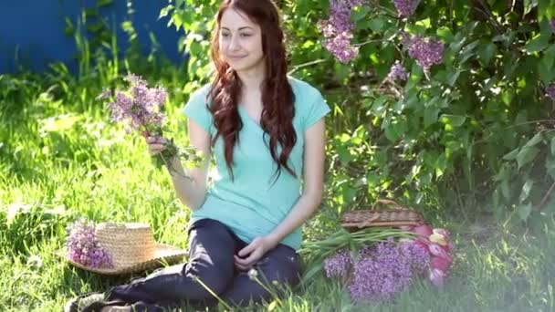 Όμορφη γυναίκα με ένα μπουκέτο από λιλά κάθεται στο πάρκο άνοιξη στο γρασίδι - Πλάνα, βίντεο
