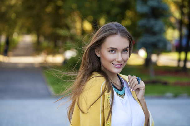 Happy young woman in yellow coat in autumn street - Foto, afbeelding