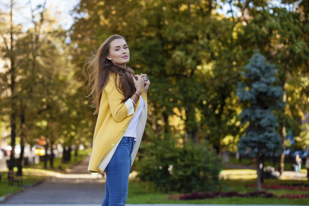 Happy young woman in yellow coat in autumn street - Foto, imagen