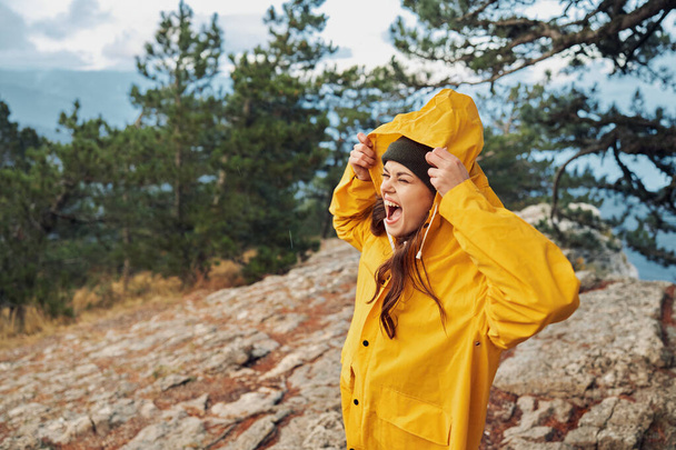 Жінка в жовтому плащі насолоджується захоплюючим видом, стоячи на вершині гори з руками на голову, подорожі, пригоди, природу, красу - Фото, зображення