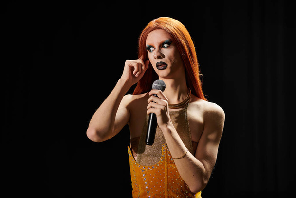 drag queen z rudymi włosami i efektowny strój posiada mikrofon, występujący na scenie. - Zdjęcie, obraz