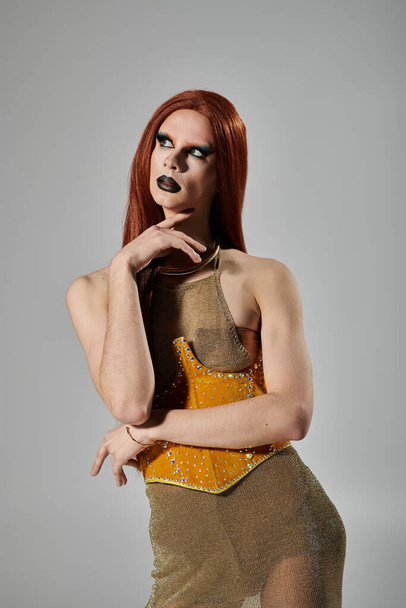 Un artiste drag pose dans une tenue glamour et dorée sur un fond gris. - Photo, image