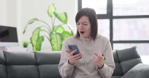 Egy nő telefonnal és bankkártyával feldúltnak és feldúltnak tűnik a kanapén ülve. Pénzlopás egy banki alkalmazásból - Felvétel, videó