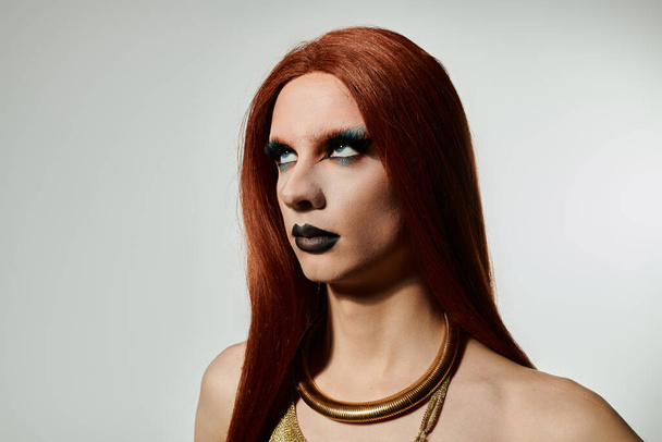 Uma drag queen posa para um retrato, exibindo um visual ousado de maquiagem e cabelo vermelho fluindo. - Foto, Imagem