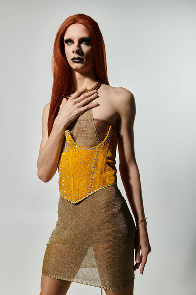 Eine Drag-Diva mit langen roten Haaren posiert in einem aufschlussreichen goldenen Kleid. - Foto, Bild