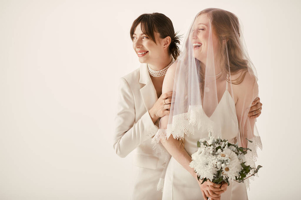 Zwei Bräute in weißen Gewändern umarmen sich an ihrem Hochzeitstag und teilen einen zärtlichen Moment der Freude und Liebe. - Foto, Bild