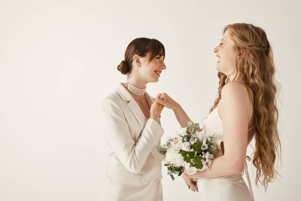 Zwei Bräute im weißen Hochzeitskleid stehen Händchen haltend und lächeln sich an. - Foto, Bild