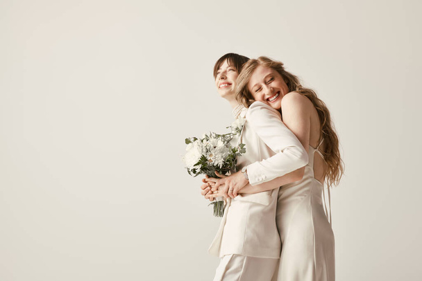 Két fehér ruhás menyasszony ölelkezik, örömük tapintható, ahogy egy csokor fehér virágot tartanak a kezükben.. - Fotó, kép