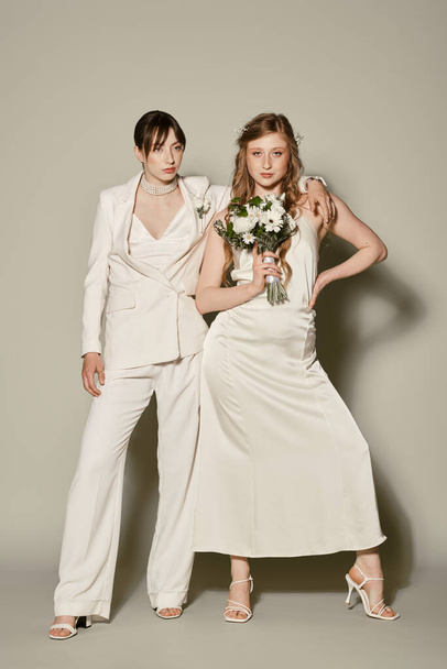 Dwie panny młode w białym stroju objąć podczas ceremonii ślubnej, świętując swoją miłość na neutralnym tle. - Zdjęcie, obraz