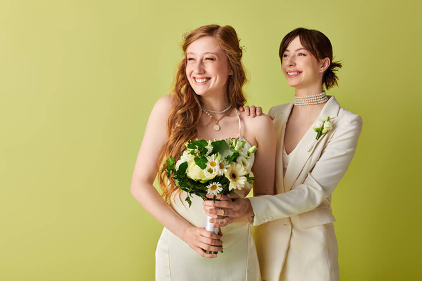 Дві жінки в білому весільному вбранні стоять на фоні зеленого кольору, б'ючись з радістю в день весілля. - Фото, зображення