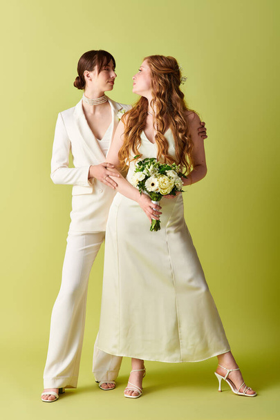 Duas mulheres de traje de casamento branco se unem em um fundo verde, sorrindo e olhando uma para a outra. - Foto, Imagem