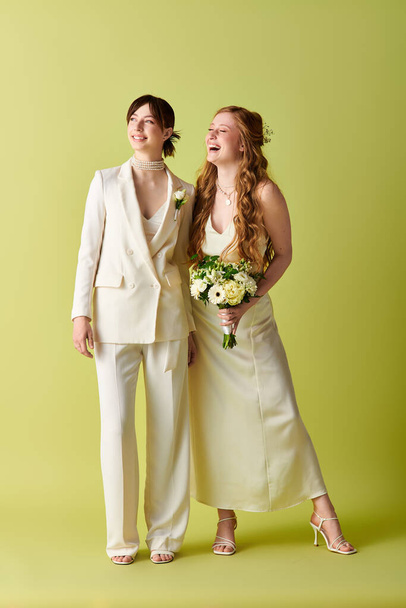Two women in white wedding attire stand together smiling against a green background. - Photo, Image