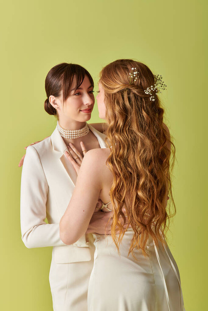 Egy fiatal leszbikus pár fehér ruhában ölelkezik az esküvőjükön, a szerelmük nyilvánvaló a tekintetükben.. - Fotó, kép