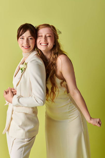 Zwei Bräute im weißen Hochzeitskleid lächeln glücklich vor grünem Hintergrund. - Foto, Bild