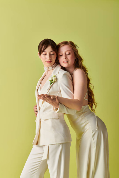 Two young women in white attire embrace during their wedding ceremony, celebrating their love against a green backdrop. - Photo, Image