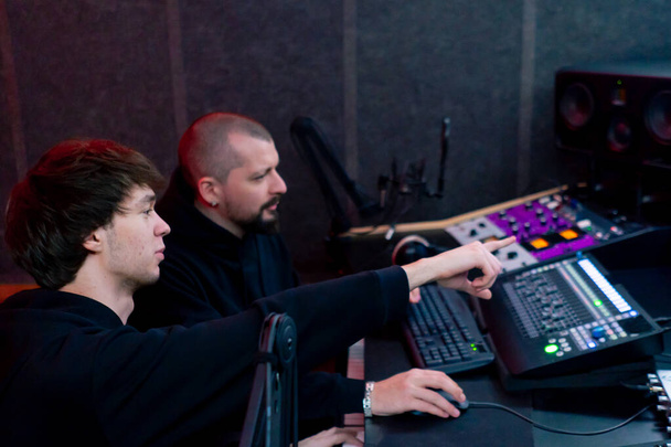 in de opnameruimte donker Met een neonverlichte studio leert een geluidsopnameapparaat zijn assistent hoe hij aan de consoles moet werken - Foto, afbeelding