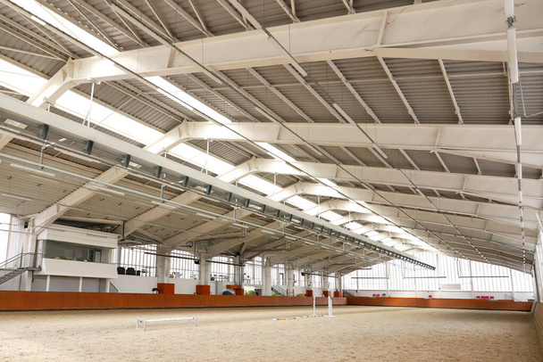 馬の訓練のための砂をカバーする現代屋内乗馬場. 広々としたライディングホールのインテリアビュー. 窓から日光. 屋内モダンなエクエストリアン - 写真・画像