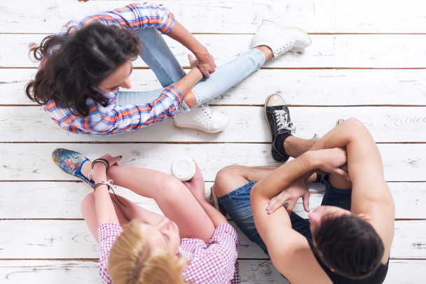Amigos dos chicas y chico sentado en el suelo en verano jeanswear calle estilo informal urbano hablando, divirtiéndose, vista superior
 - Foto, imagen