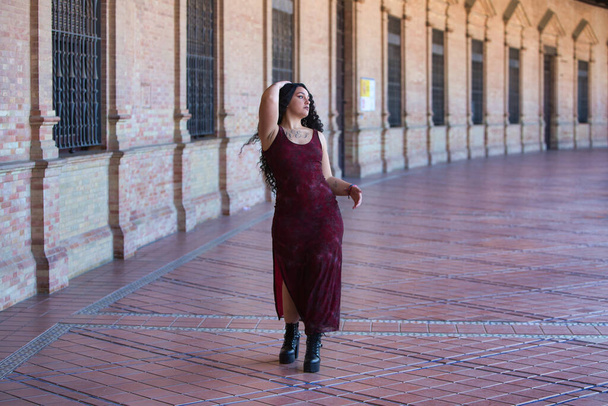 Latinalainen nainen, nuori, kaunis ja rasvainen käyrät ja pitkät kiharat ruskeat hiukset, elegantti pitkä mekko kävelee välillä kaaria Plaza Espana Sevillassa tekee erilaisia asentoja ja asentoja - Valokuva, kuva