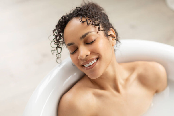 Ontspannen latijnse dame liggend in schuimig bad, ontspannen met gesloten ogen, baden thuis in de badkamer, vrije ruimte - Foto, afbeelding