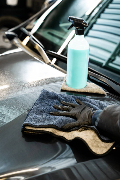Professional car valeting. Wiping vehicle after applying spray of quick detailer to make car surface clean and shining. Polishing car body using microfiber cloth - Photo, Image