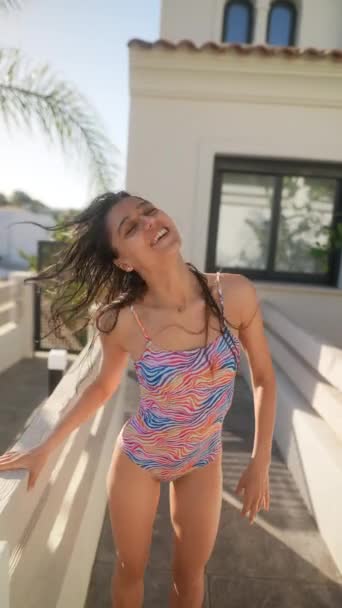 A young woman wearing a colorful swimsuit enjoys a sunny day at the poolside. Captured in motion with natural light. - Footage, Video