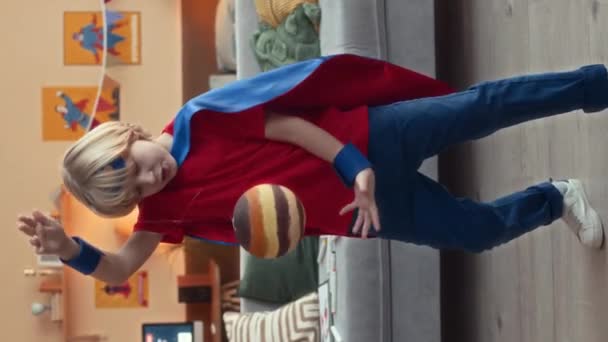 Vertikální plný záběr kavkazského chlapečka oblečeného v kostýmu superhrdiny, jak si hraje s ručně vyrobenou planetou visící na tenké čáře, zatímco zůstává doma během volného času - Záběry, video