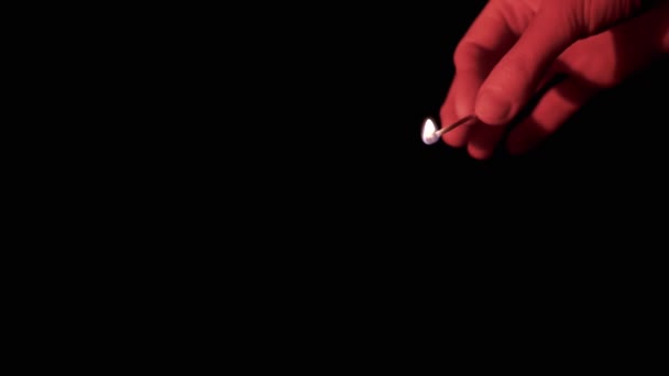 Hand Holds a Burning Match in Red Lighting on a Black Background in Empty Space. Vista lateral. Um fósforo ardente na mão queima com uma chama brilhante. Close-up, câmara lenta. Isolado. Quarto escuro. - Filmagem, Vídeo