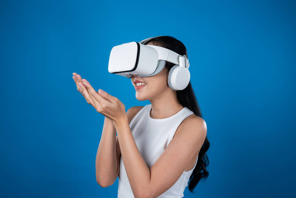 Donna intelligente in piedi con sfondo blu con auricolare VR che collega la tecnologia metaversa e futuristica della comunità del cyberspazio. Elegante donna eccitato vedendo generato scenario virtuale. Allucinazioni. - Foto, immagini