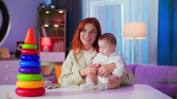 portrét mladé ženy s malým dítětem hrající si s barevnými hračkami na kameře při nahrávání video blogu pro sociální sítě v útulné místnosti - Záběry, video