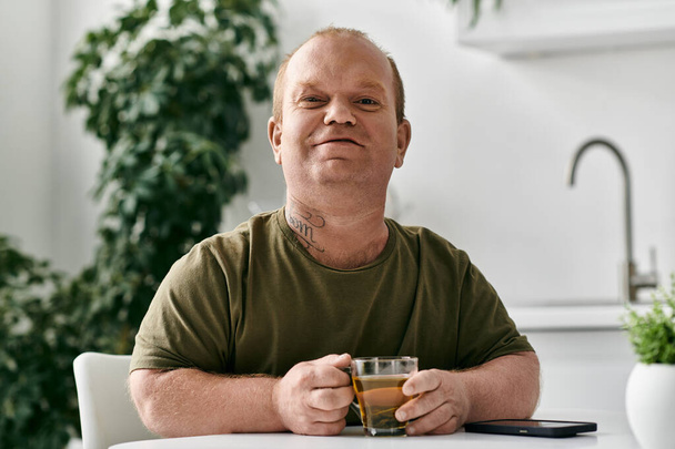 Muž s inkluzivitou sedí u stolu, drží šálek čaje, ve svém útulném domově. - Fotografie, Obrázek