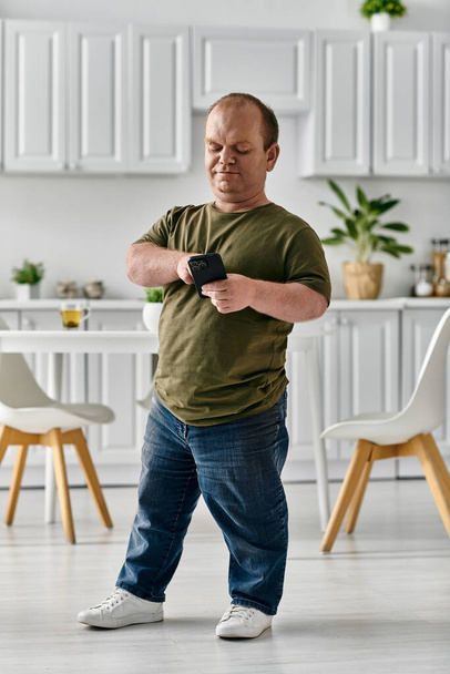 Un homme avec inclusivité en tenue décontractée se tient dans sa maison, regardant son téléphone. - Photo, image