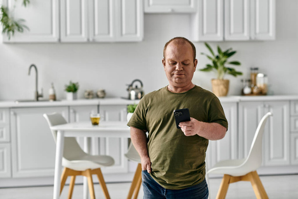 Чоловік з інклюзивністю стоїть на своїй кухні, випадково одягнений і дивиться на свій телефон. - Фото, зображення