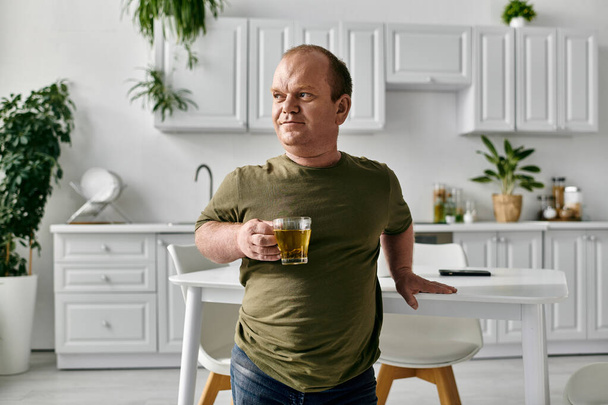 Egy alkalmi ruhába öltözött férfi áll egy modern konyhában, kezében egy csésze teával és figyelmes.. - Fotó, kép