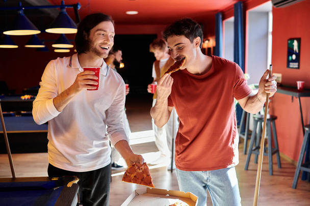 Friends enjoy a break from their billiards game, eating pizza and drinking beverages. - Photo, Image