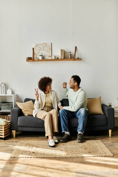 Una pareja afroamericana se sienta en un sofá en su casa, comunicándose con el lenguaje de señas. - Foto, Imagen