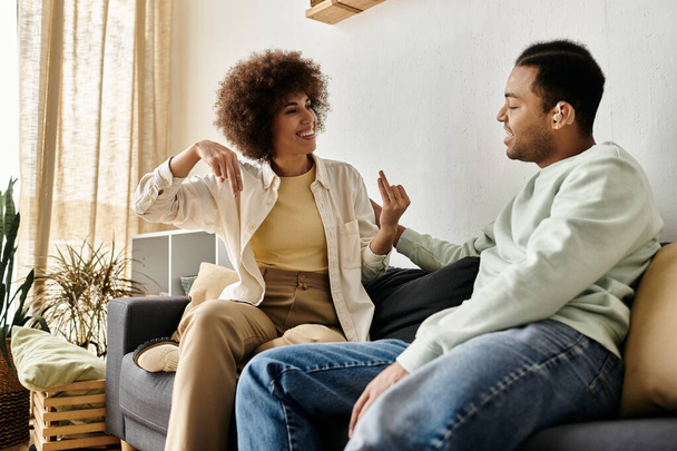 Młoda para Afroamerykanów siedzi na kanapie w domu i prowadzi ożywioną rozmowę używając języka migowego.. - Zdjęcie, obraz