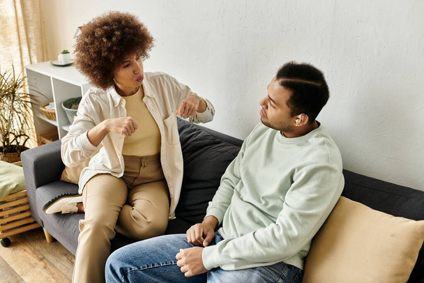 アフリカ系アメリカ人のカップルがソファに座り,シグナル言語を使ってコミュニケーションをとる. - 写真・画像