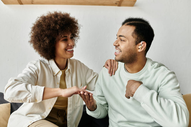 Afro-Amerikalı bir çift işaret diliyle iletişim kuruyor. Evlerinde bir kanepede otururken gülümsüyor ve gülüyorlar.. - Fotoğraf, Görsel