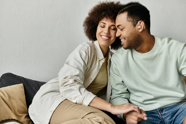 Een aantrekkelijk Afro-Amerikaans echtpaar zit dicht bij elkaar op een bank thuis. - Foto, afbeelding