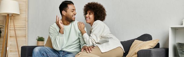 Una joven pareja afroamericana usa lenguaje de señas para comunicarse mientras se relaja en un sofá en casa. - Foto, imagen
