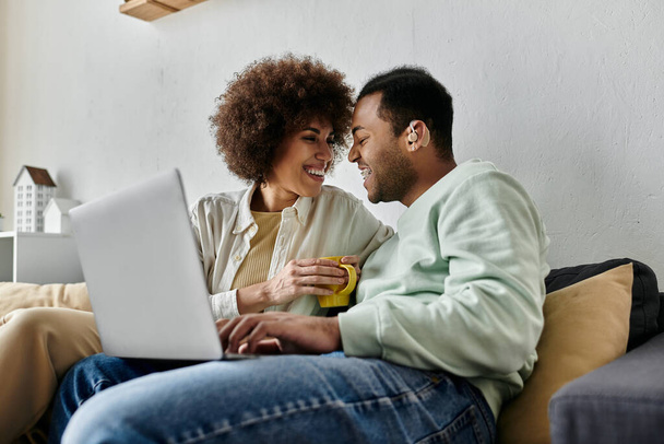Kaunis afroamerikkalainen nainen istuu miehensä lähellä kuulolaitteen kanssa ja katselee kannettavaa tietokonetta. - Valokuva, kuva