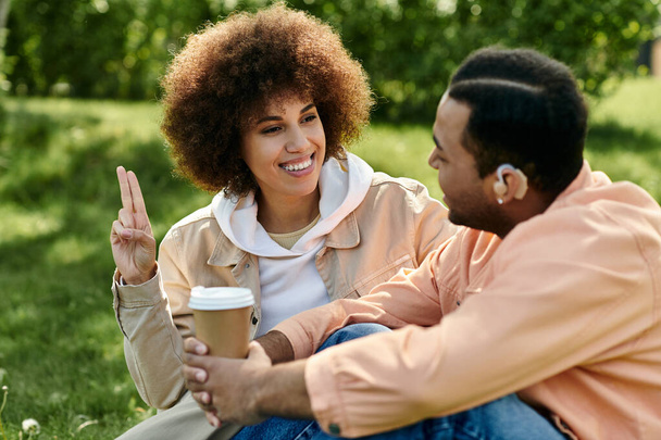 Un couple afro-américain communique par le langage des signes tout en étant assis ensemble dans un parc. - Photo, image