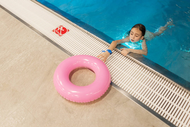 Zbliżenie portret małej pływaczki odpocząć po kąpieli w basenie. Mała dziewczynka boi się utonąć w wodzie. Odbiór. Koncepcja bezpieczeństwa dzieci w pobliżu wody basenowej. - Zdjęcie, obraz