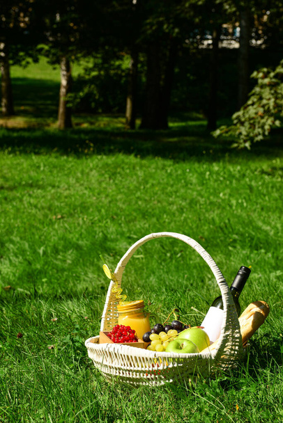 Плетеная корзина с вкусной едой и напитками для романтического пикника на траве в парке - Фото, изображение