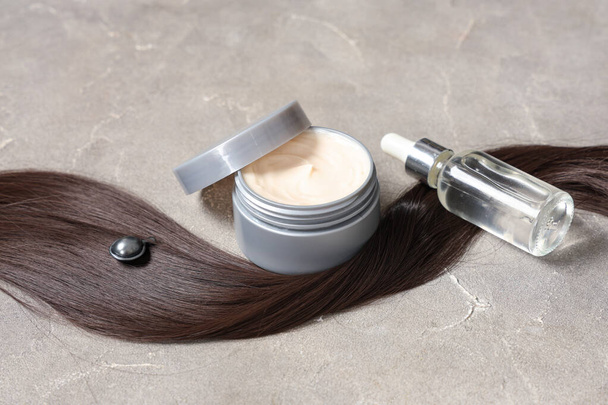 Braune Strähne mit Haarmaske, Kapsel und Flasche Kosmetiköl auf grauem Grunge-Hintergrund, Nahaufnahme - Foto, Bild