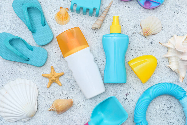 Красивая композиция с солнцезащитным кремом и пляжными аксессуарами для детей на сером пятнистом фоне - Фото, изображение